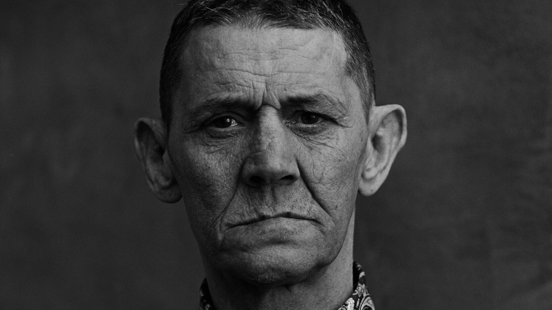 A man dressed in a patterned shirt stares at the camera.