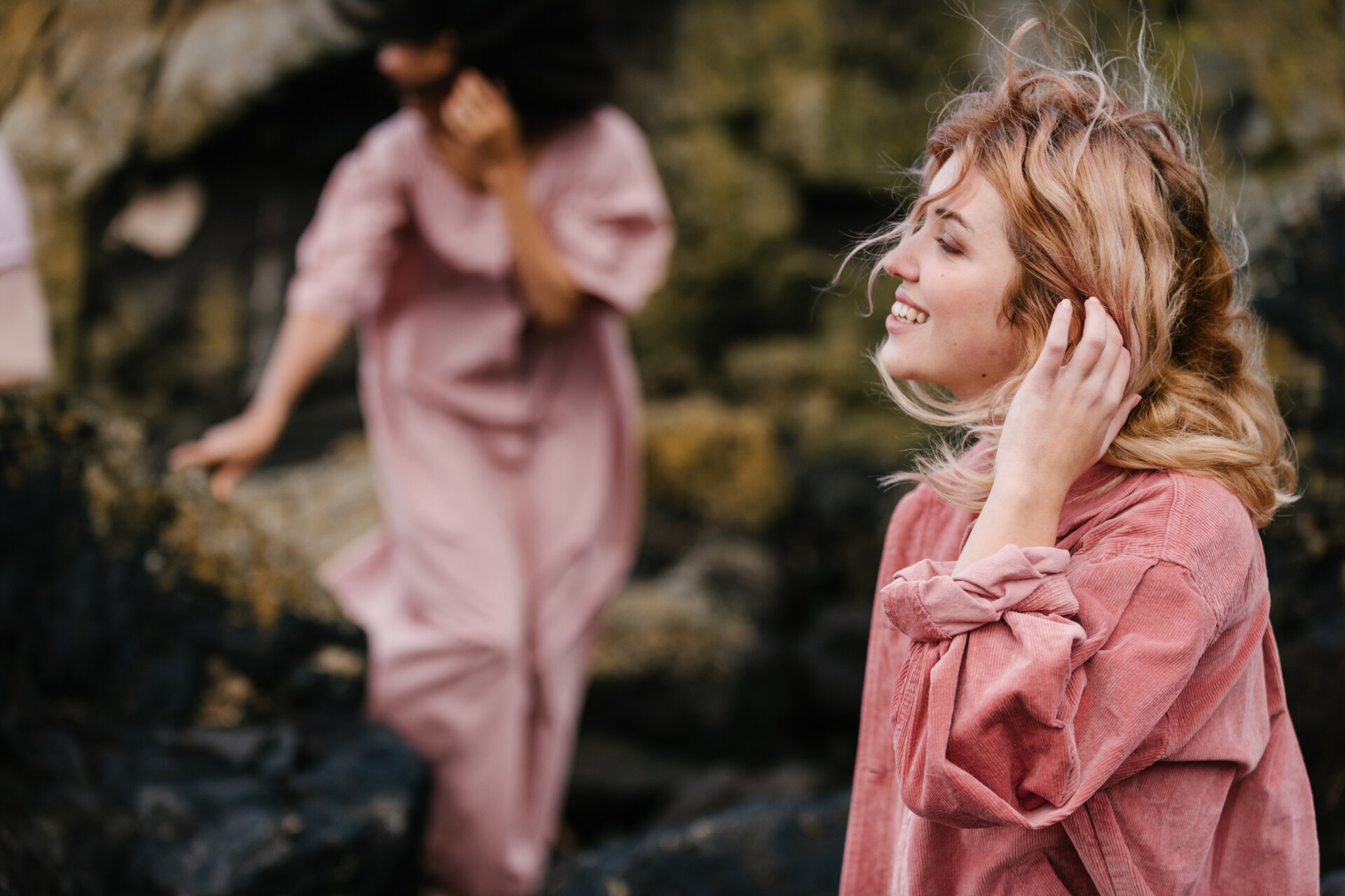A woman in a pink shirt holding her hand to her face as her hair is blown in the wind.