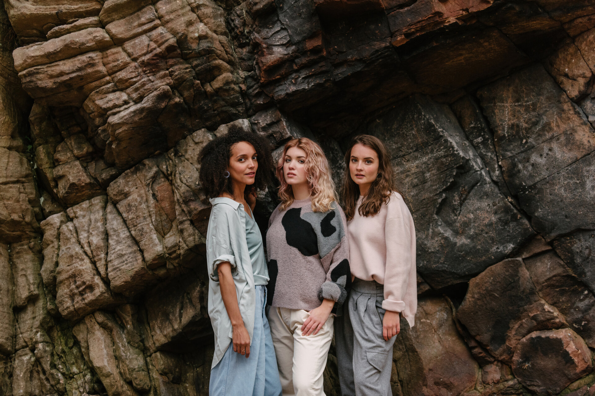Three women standing close together in front of a rock face. They are all looking at the camera.