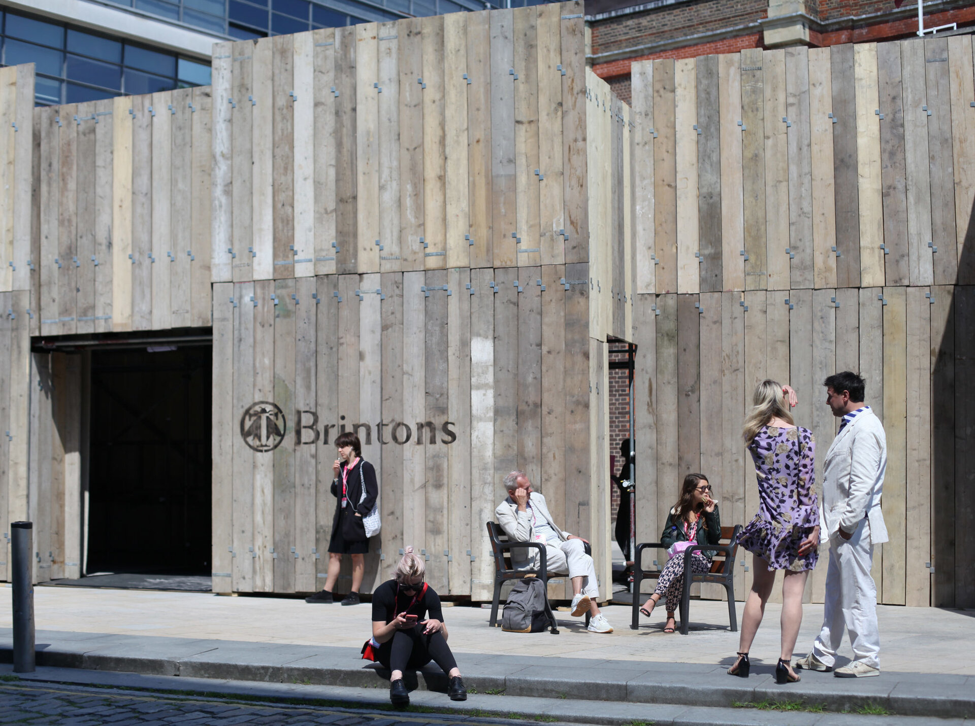 People standing outside of a wooden structure in the sunshine.
