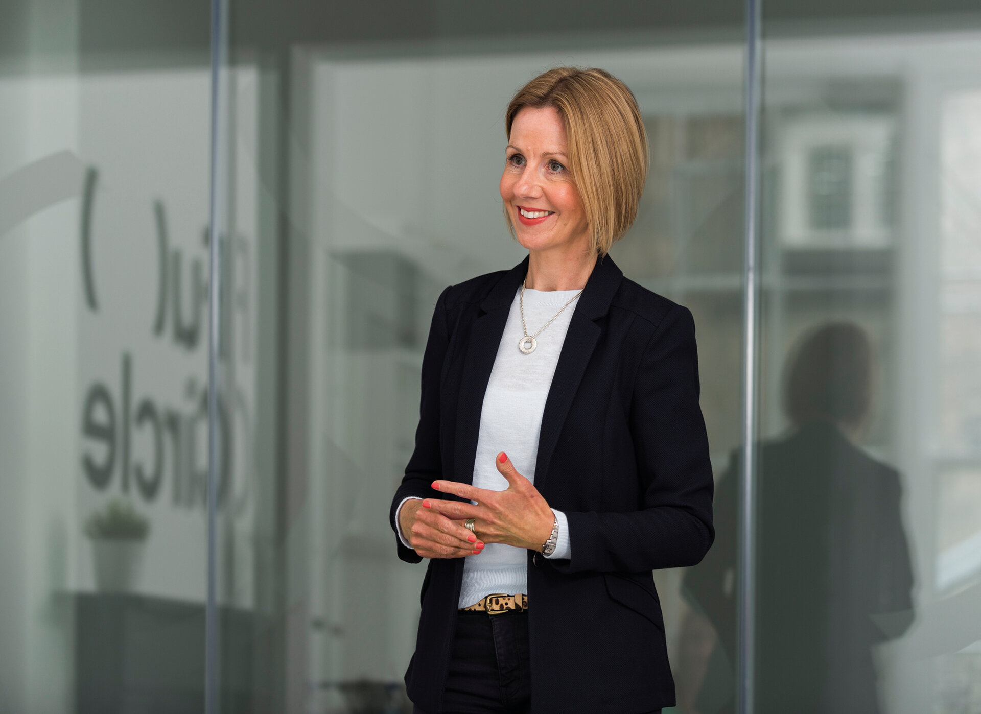 A woman stands in front of a window looking into the room and smiling.