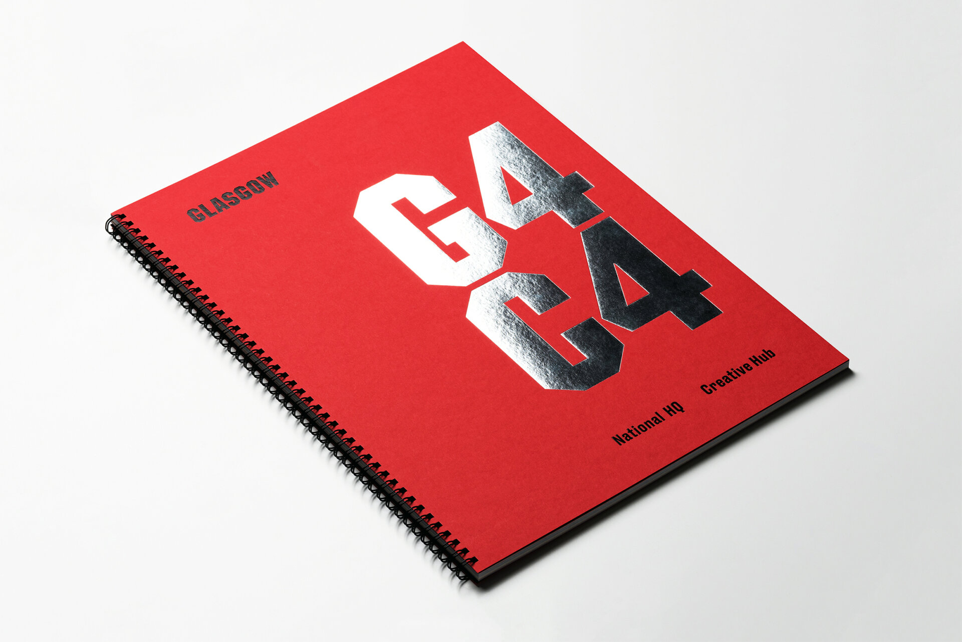 A red wire bound book that has silver foiled text on the front that reads "G4C4" sitting on a white surface.