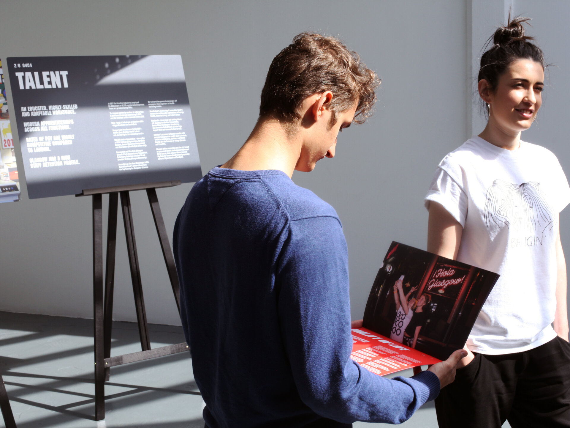 Two people standing in a brightly light space, reading a document.