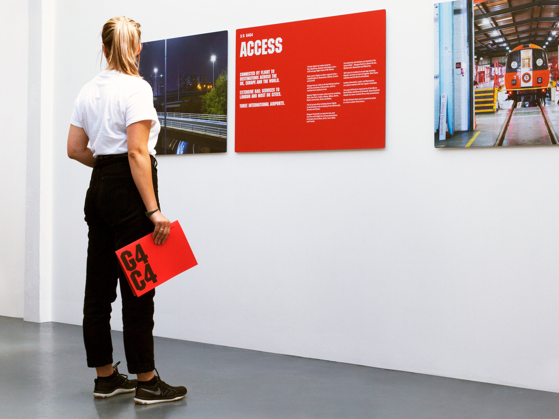 A woman standing in front of a red exhibition board. She is holding a red document.
