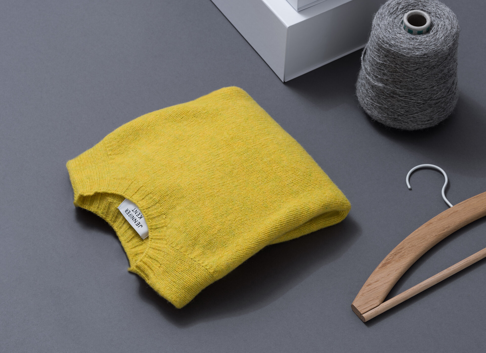 A yellow jumper siting with a wooden hanger and grey loom.