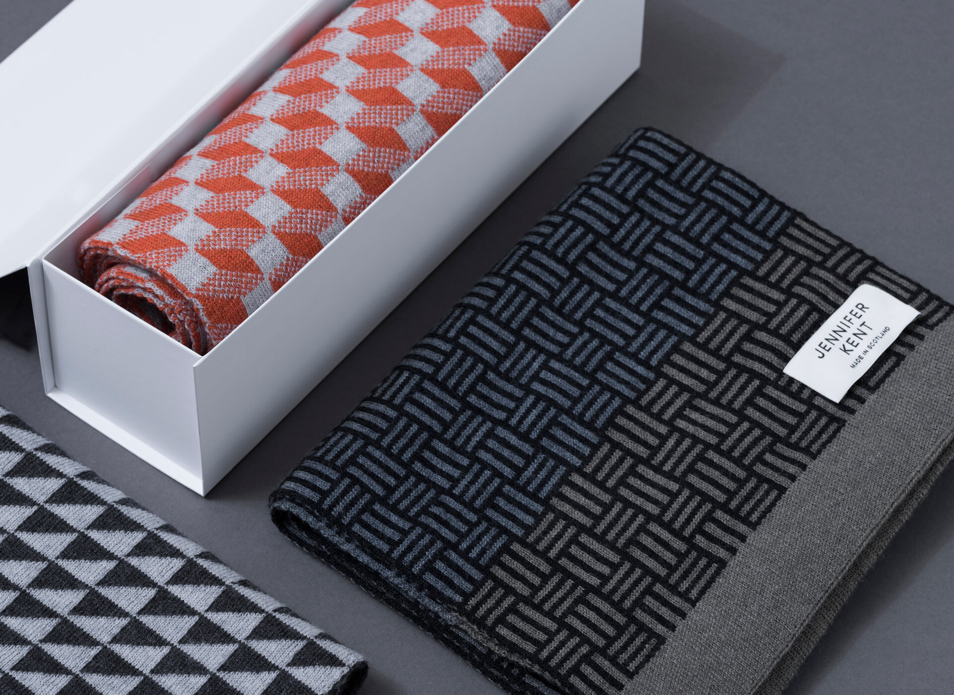 A white box with an orange patterned scarf sitting next to a black and grey patterned scarf.