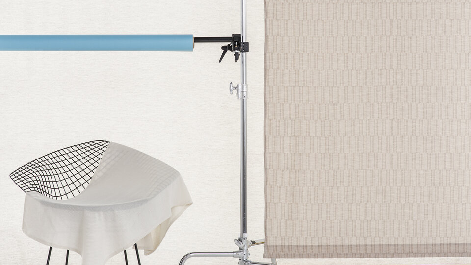 A piece of lace fabric lies across a wire chair. There is a large panel of fabric beside it.